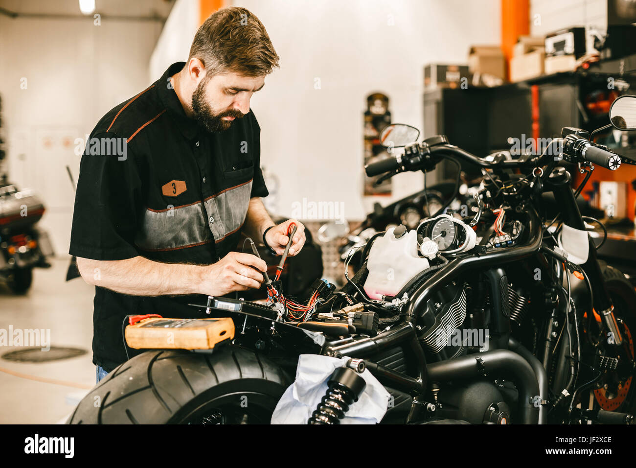 Confident young man repairing motorcycle in repair shop - electronics repair. This bike will be perfect. Stock Photo