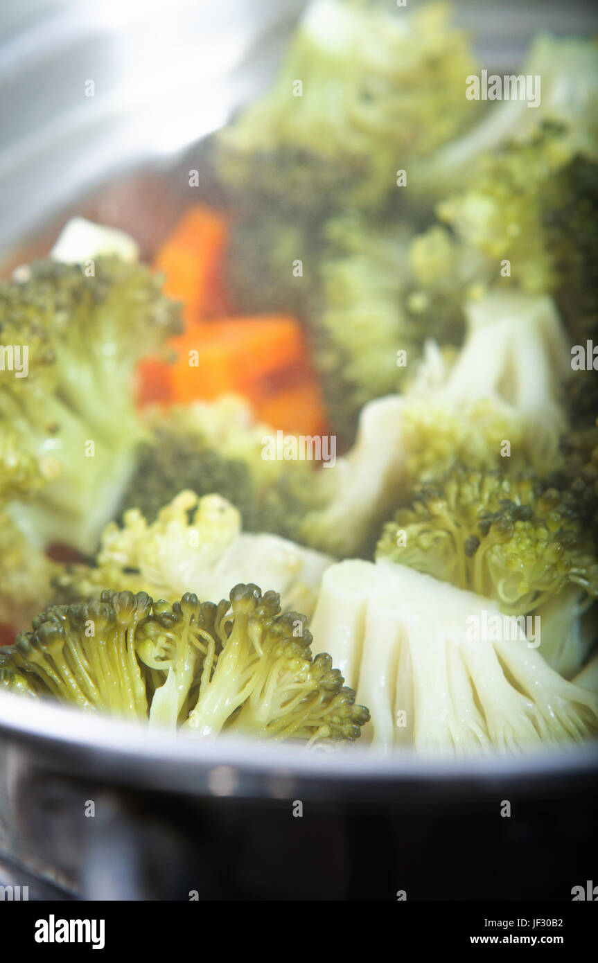 Broccoli florets and carrots cooking in a steamer, with steam visible.  Vertical (portrait) orientation. Stock Photo