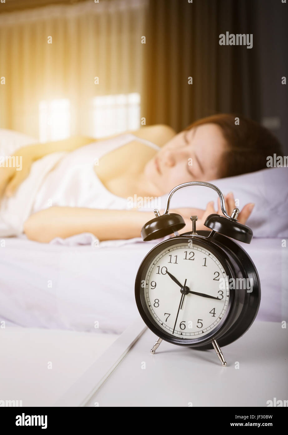 clock show 10 am. and woman sleeping on bed with sunlight in the