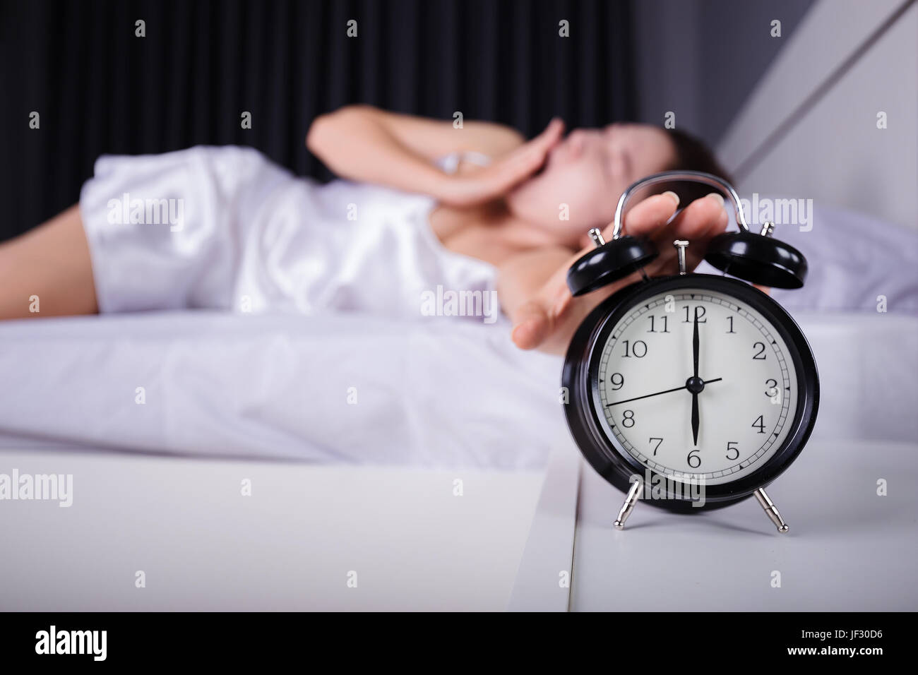 woman sleeping and wake up to turn off the alarm clock in the morning