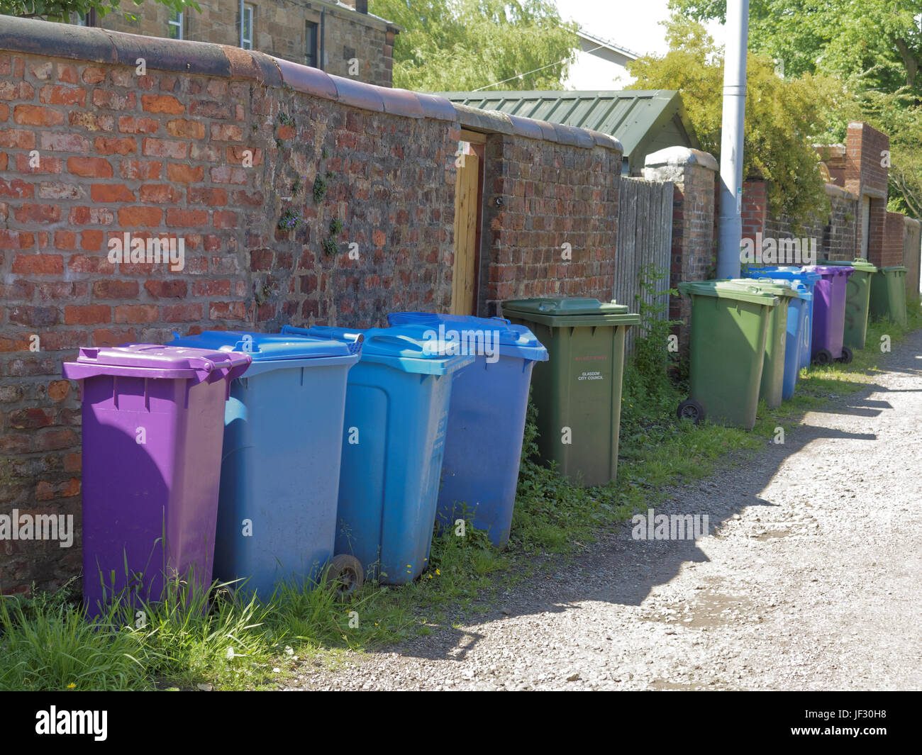 line of coloured refuse bins neat tidy clean in drive alley backstreet cobbles sunny Stock Photo