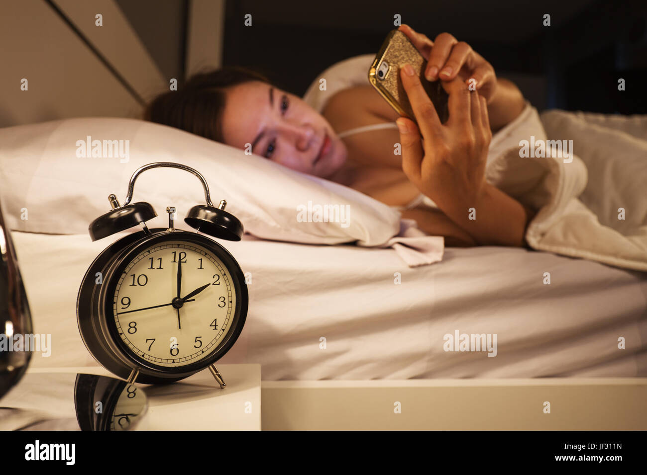 clock show 2 O'clock and woman using her smartphone on bed in the
