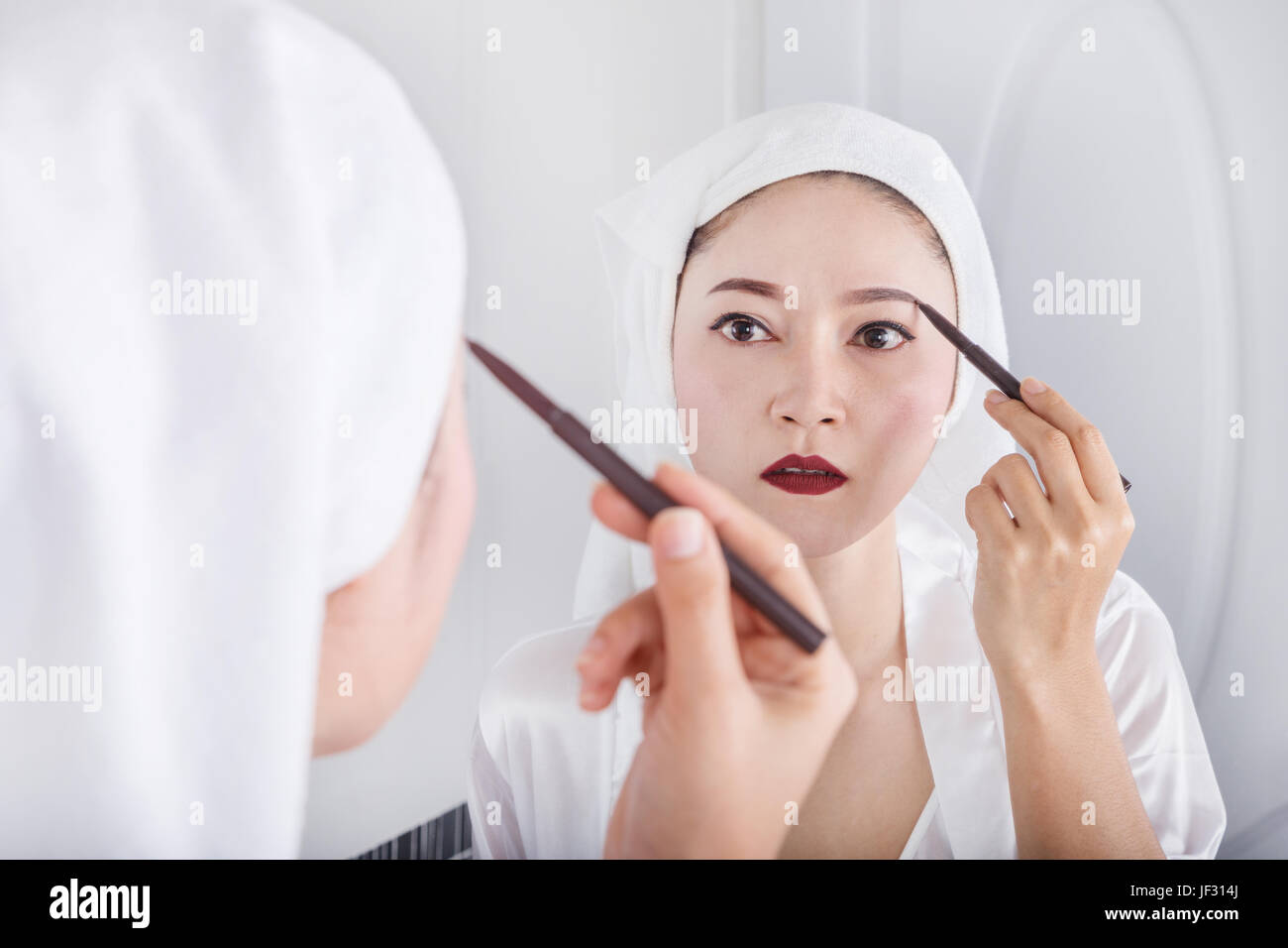 Beautiful woman looking mirror and using pencil makeup eyebrow Stock
