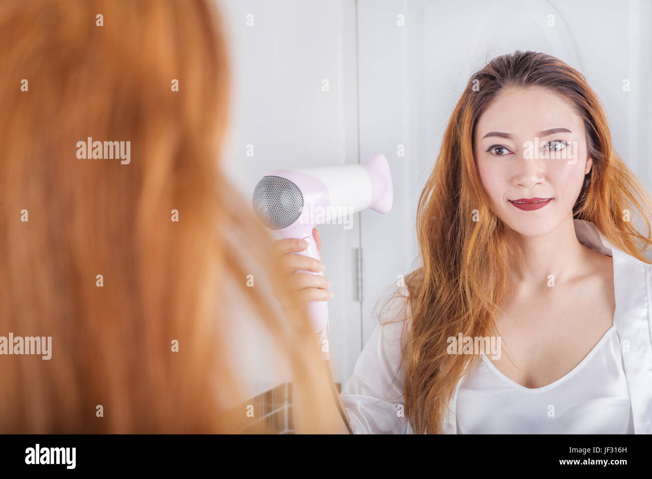 woman looking in the mirror drying her hair in bathroom Stock Photo