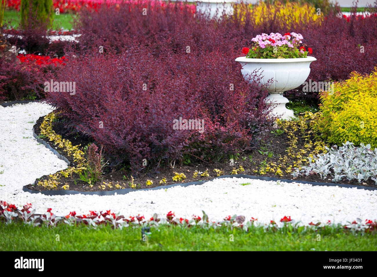 Decorative flowerbed with multi-colored shrubs with ceramic vases with geraniums Stock Photo