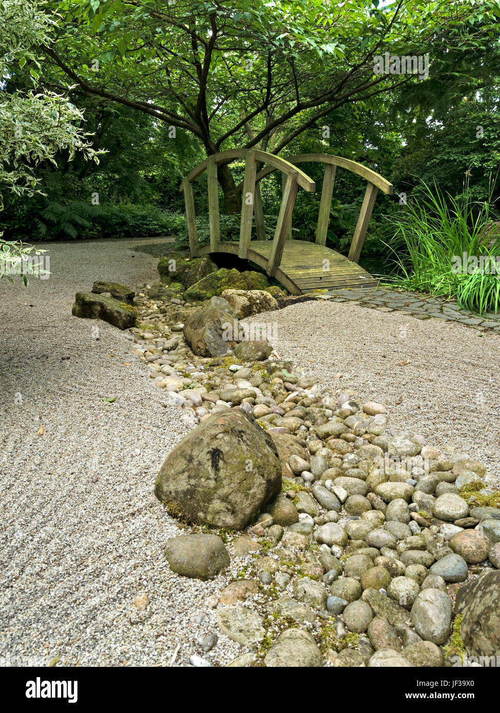 Japanese Zen styled garden with raked gravel, ornate wooden bridge and river of pebbles, Barnsdale Gardens, Rutland, England, UK. Stock Photo