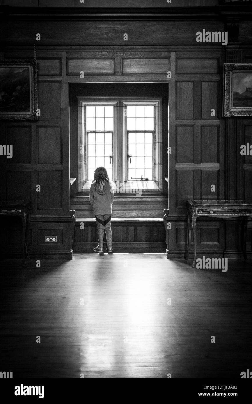 Girl looking out of the window inside Bamburgh Castle, Northumberland, England, UK Stock Photo