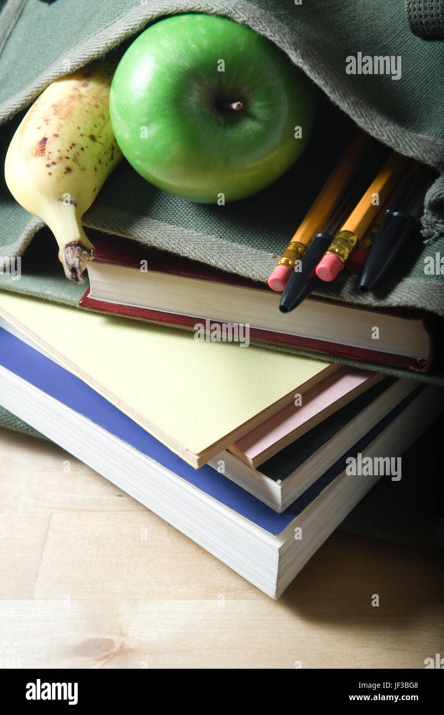 An open school satchel, containing books, pens, pencils and fruit.  Vertical (portrait) orientation. Stock Photo