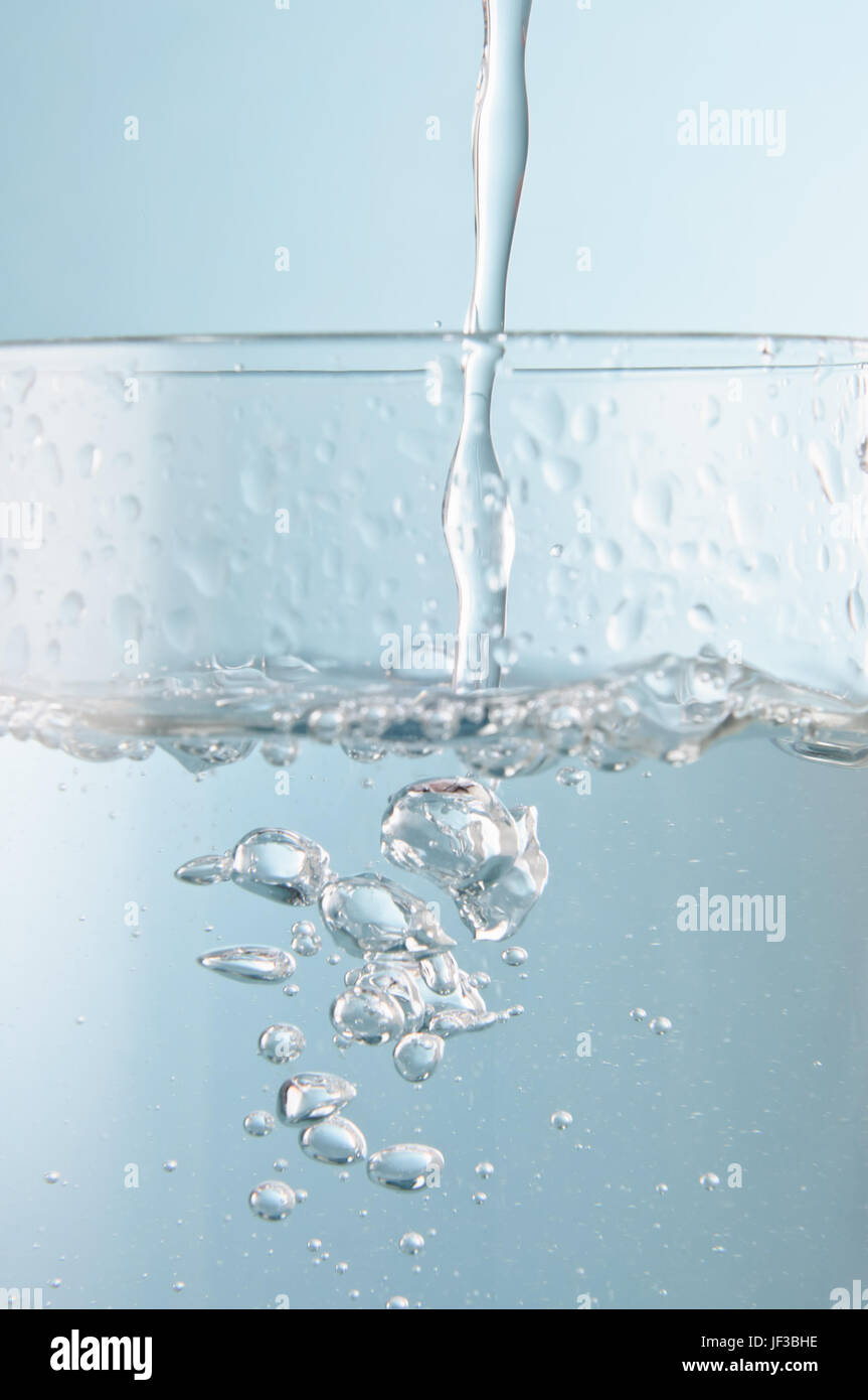 Vertical action shot of water pouring into a glass against an icy blue background.  Close up (macro). Stock Photo
