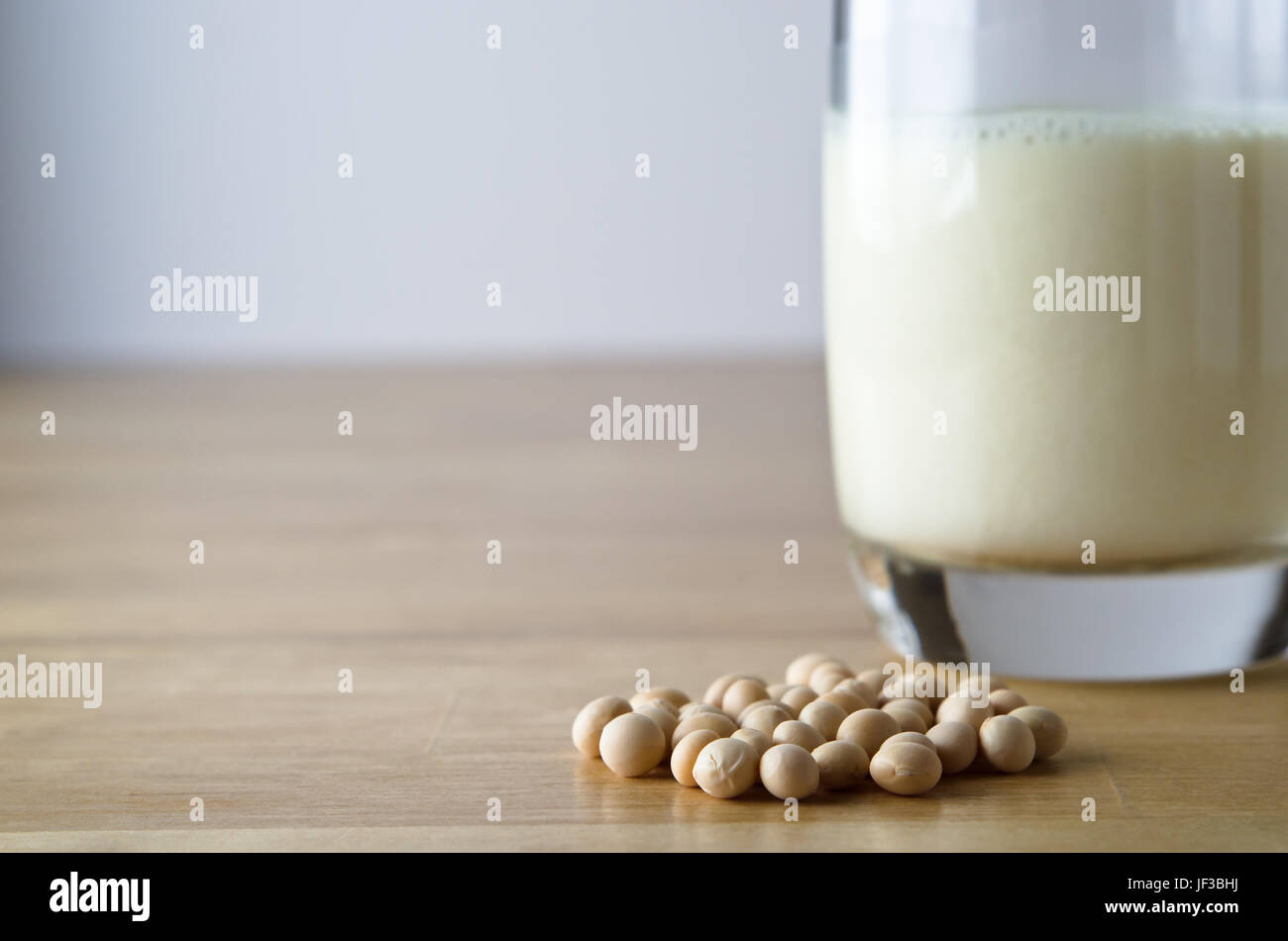 Dry soya (soy) beans with glass of soya milk in soft focus background on a light wooden table.  Horizontal (landscape) orientation. Stock Photo