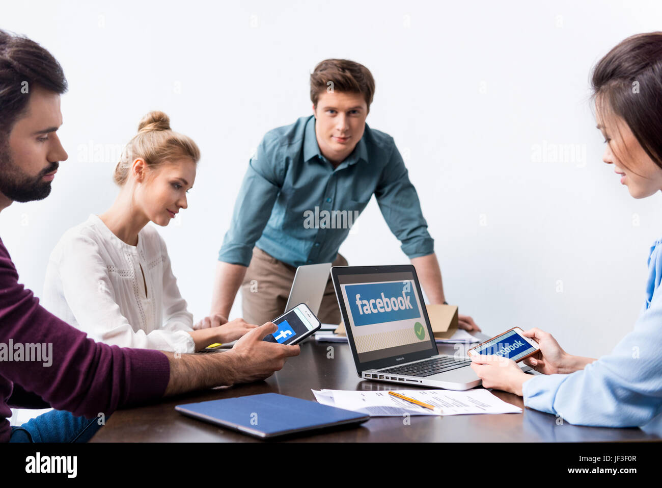 Young businesspeople using digital devices with facebook logo icons on ...