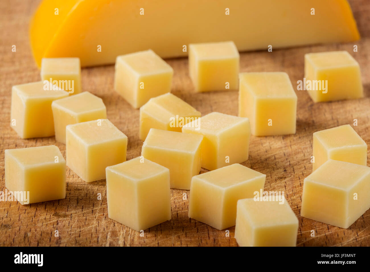 Close up of cubes of yellow cheese stacked randomly on wooden chopping board Stock Photo