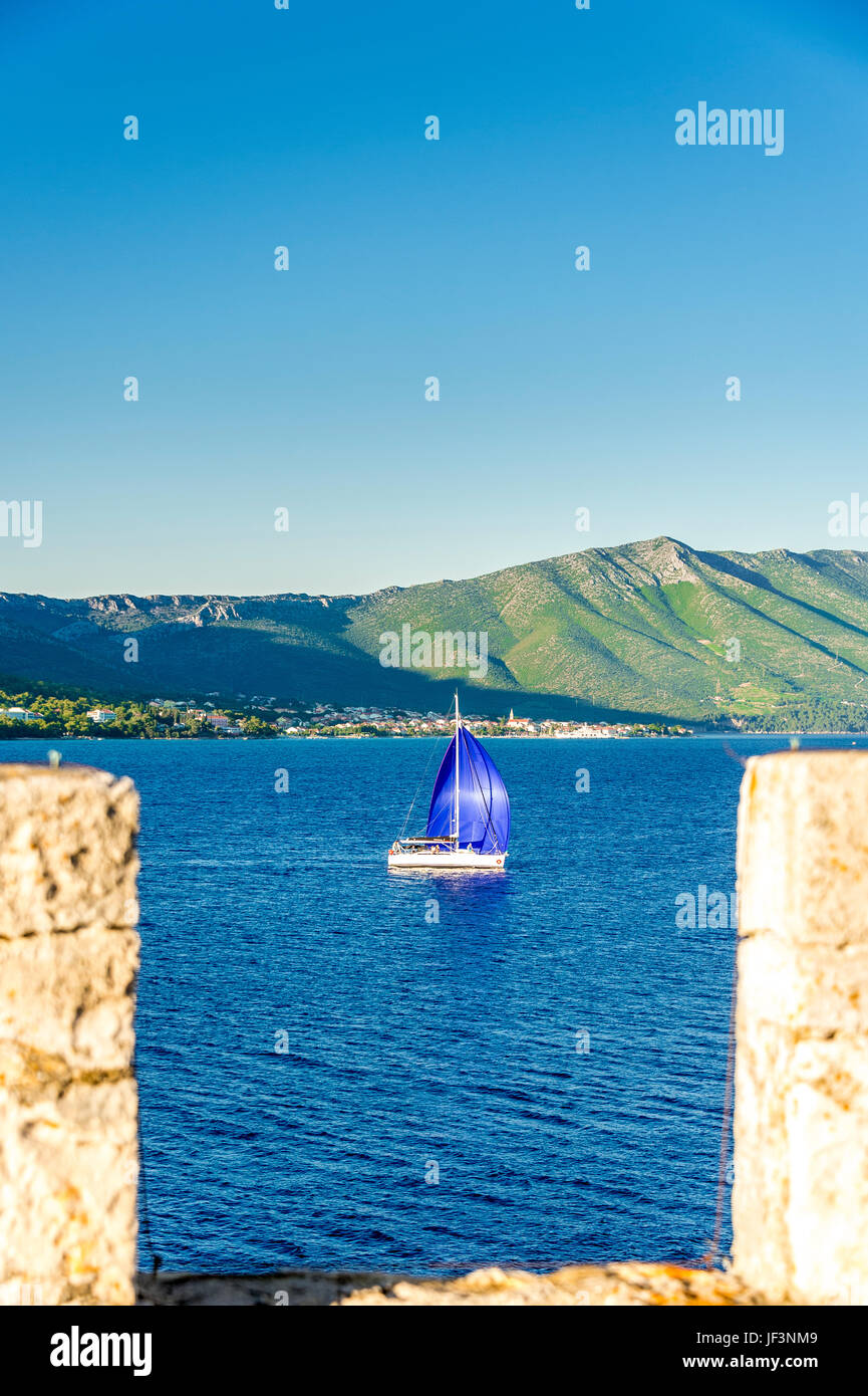 A yacht sails past Korcula Town (old city) with Sveti Ilija in the background. Croatia Stock Photo