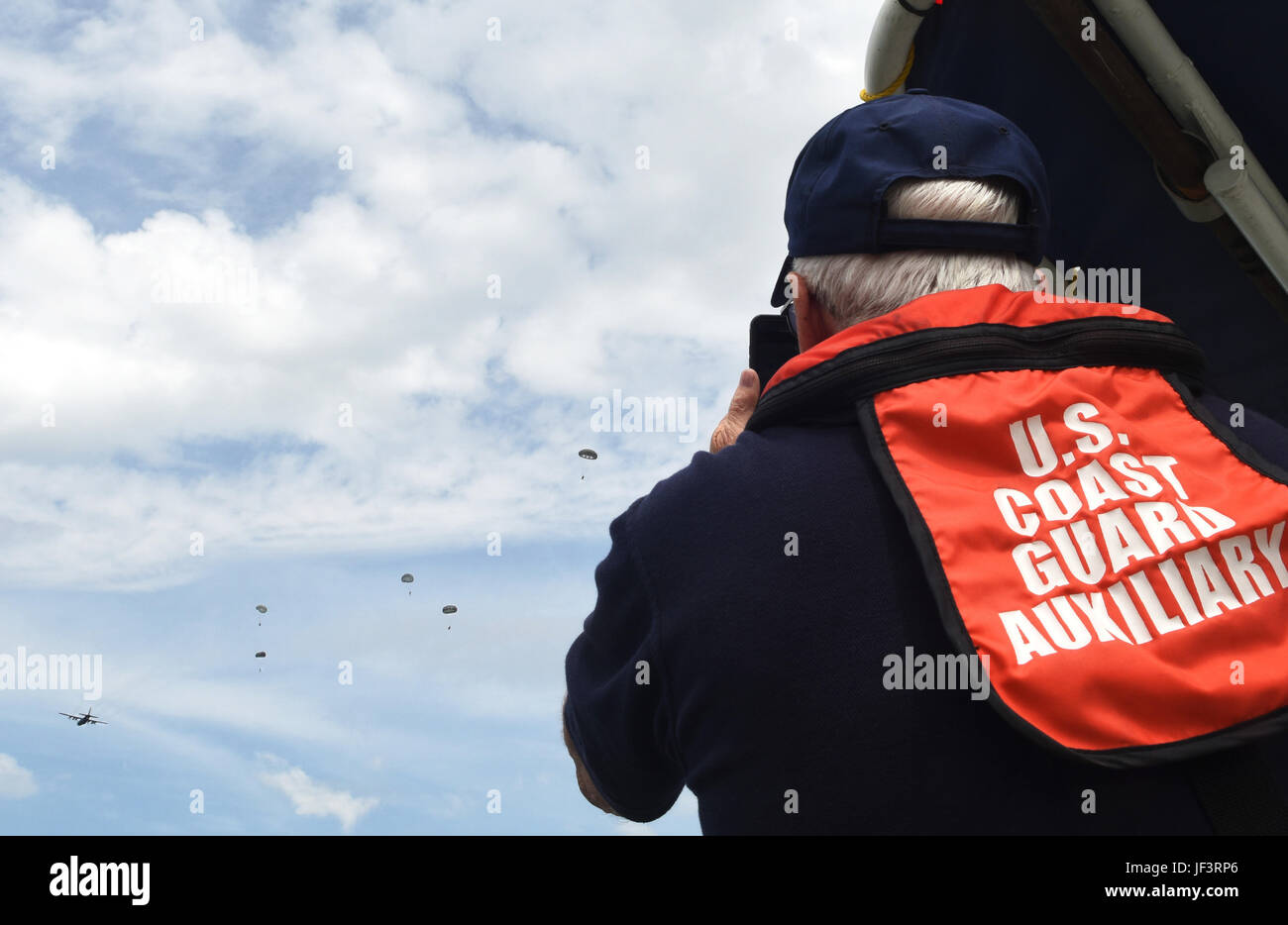 A member of the U.S. Coast Guard Auxiliary watches as members of the 181st Weather Flight parachute out of a C-130 Hercules during a deliberate water drop into Lake Worth in Forth Worth, Texas, May 20, 2017. The Coast Guard Auxiliary provided boat support to aid in parachute and jumper recovery, and provided medevac capabilities if necessary. (Texas Air National Guard photo by Staff Sgt. Kristina Overton) Stock Photo