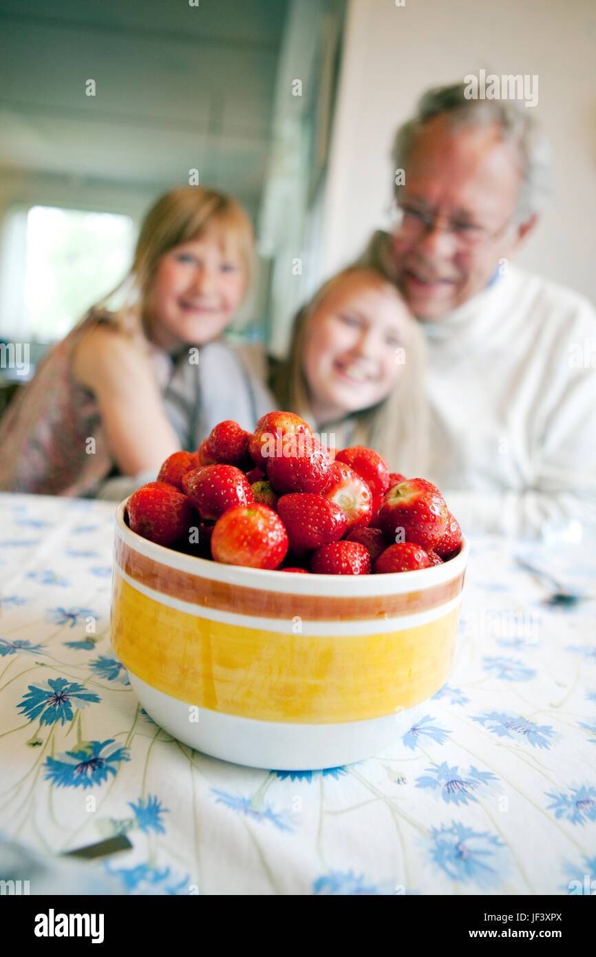 Strawberries in bowl, grandfather with granddaughters on background Stock Photo