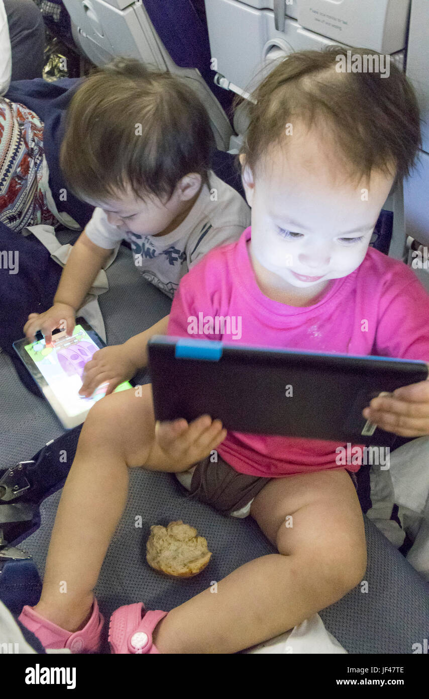 twin babies playing with tablets on airplane flight Stock Photo