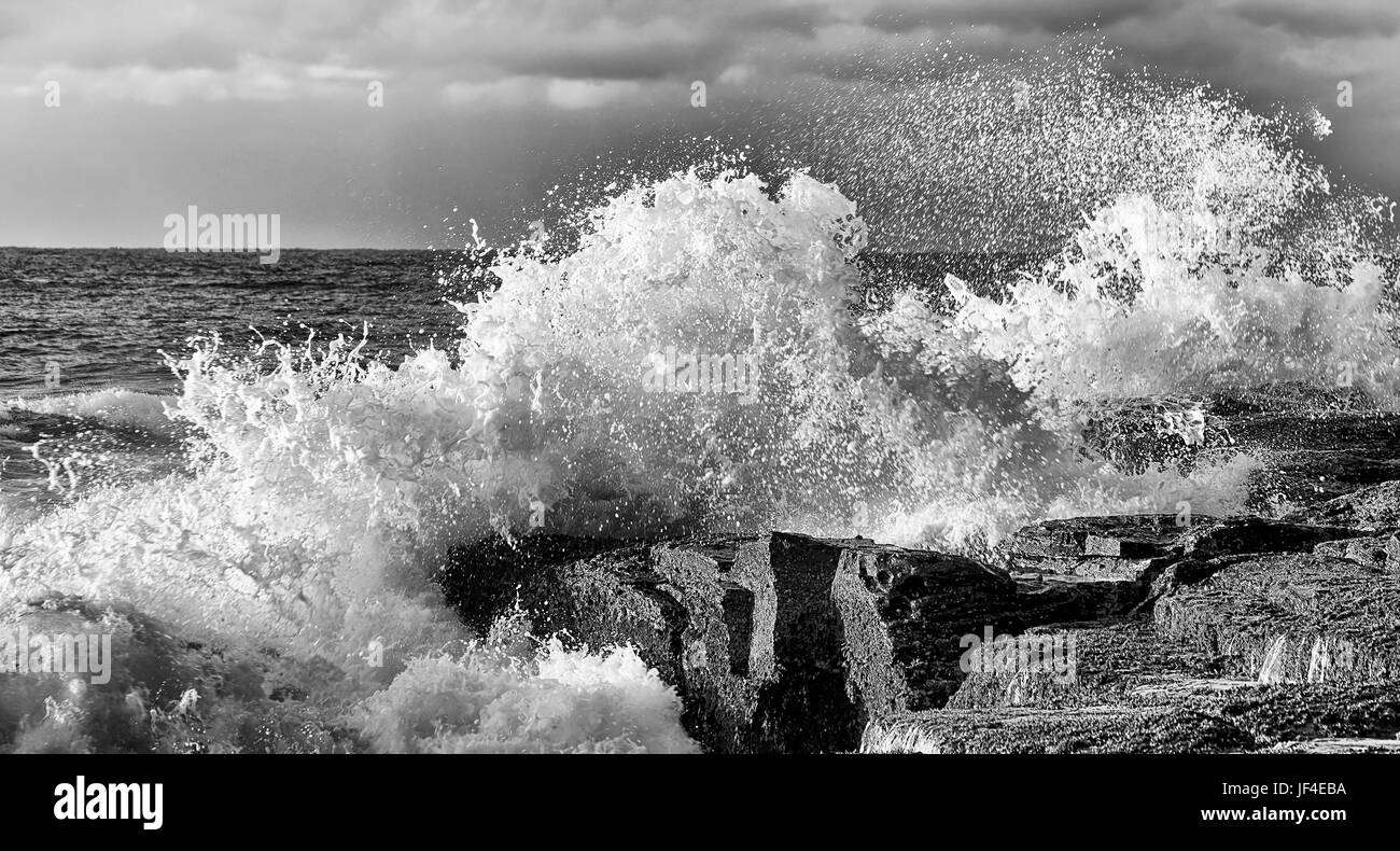 Dramatic stormy waves hit sandstone rocks at Sydney northern beaches coast of Pacific ocean. Rolling mighty waters streaming ashore. Stock Photo