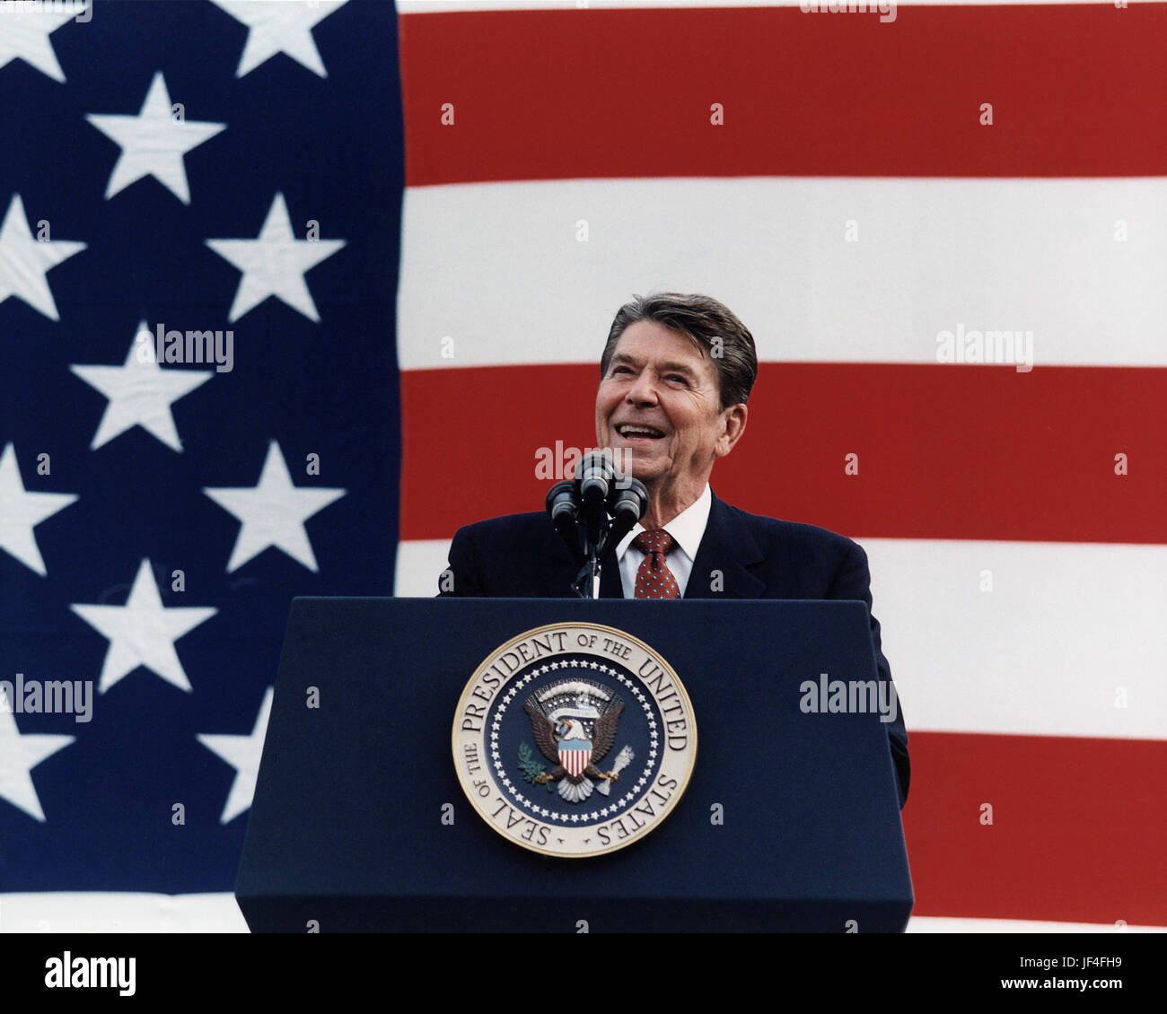 President Ronald Reagan speaks from the presidential podium before a huge American flag. Stock Photo