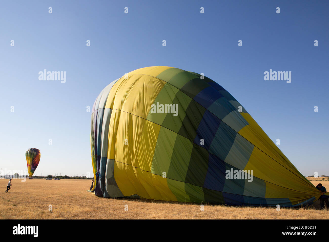 Several people deflate hot air balloons in an open field. Stock Photo