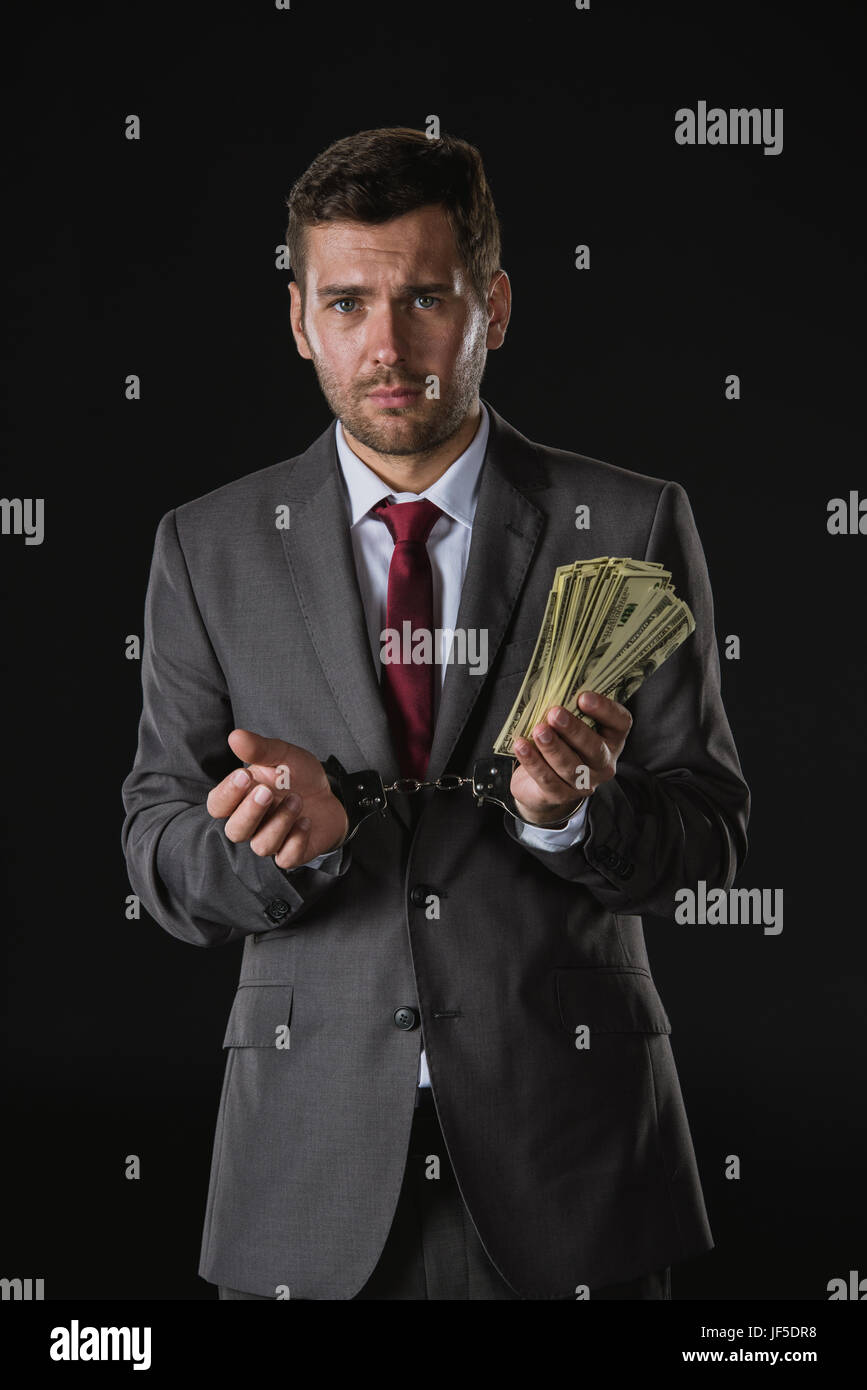 portrait of scared businessman in handcuffs holding money isolated on black, corruption concept Stock Photo