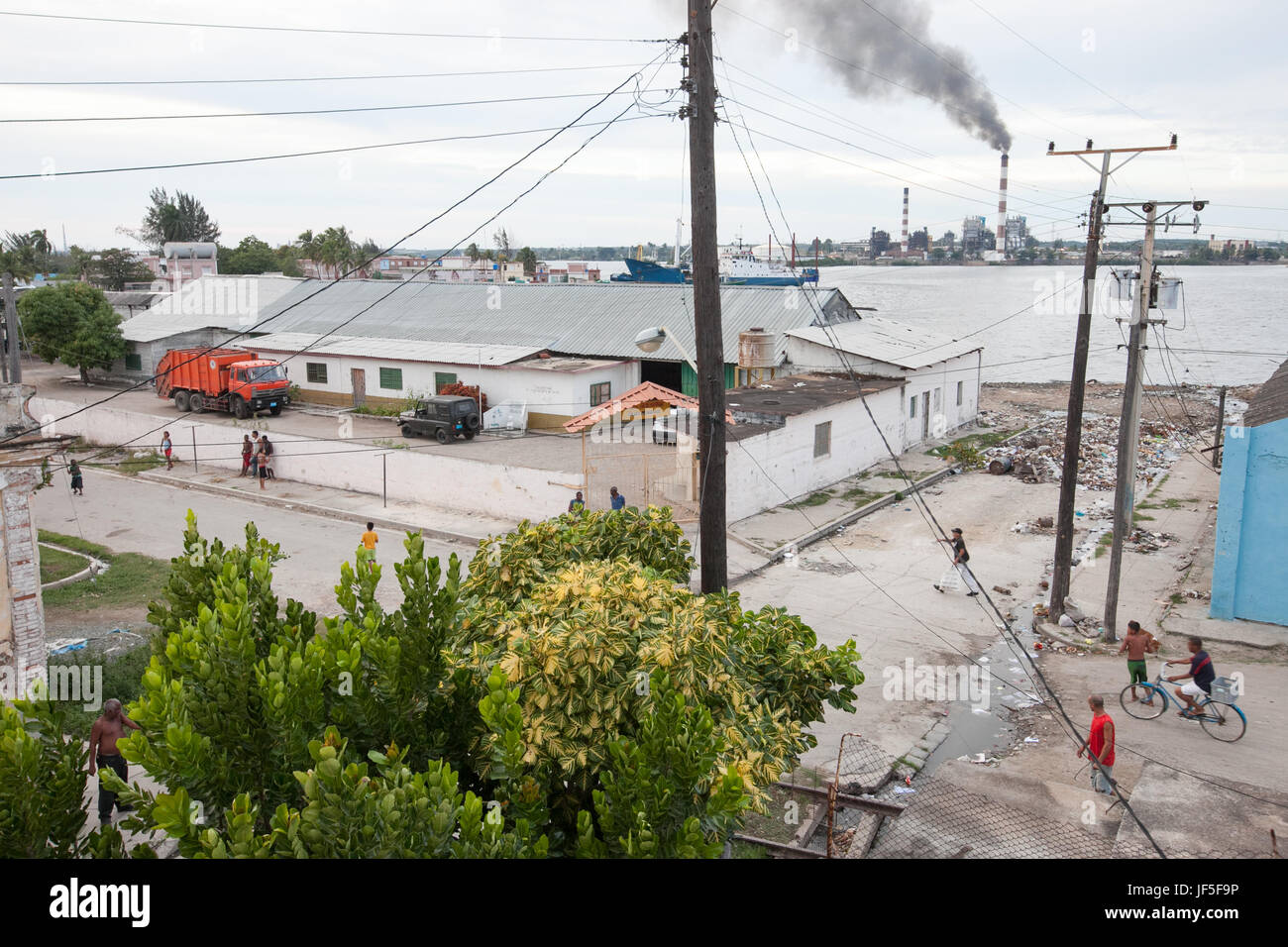 Near a port and industrial area in Cienfuegos, people walk the streets and some garbage covers a road. Stock Photo