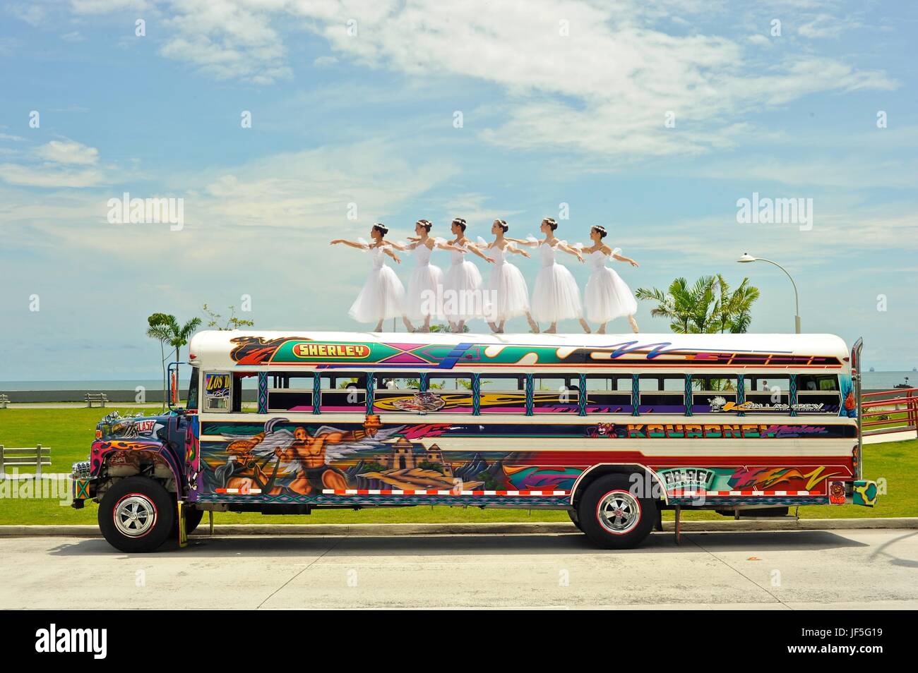 Six ballerinas dance and balance on top of a Diablo Rojo bus on La Cinta Costera, Panama's coastal highway. Stock Photo