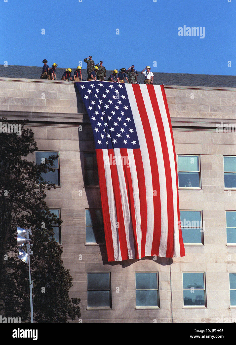 010912-D-9880W-085 Fire fighters and military personnel on the roof of the Pentagon unfurl a large American Flag during the Sept. 12, 2001, visit of President George W. Bush to the site of the previous dayÕs terrorist attack on the Pentagon.  As the flag was draped over the wall, just south of the site where American Airlines Flight 77 impacted the building, the disaster workers gathered around the President began to sing God Bless America.  DoD photo by R. D. Ward. Stock Photo