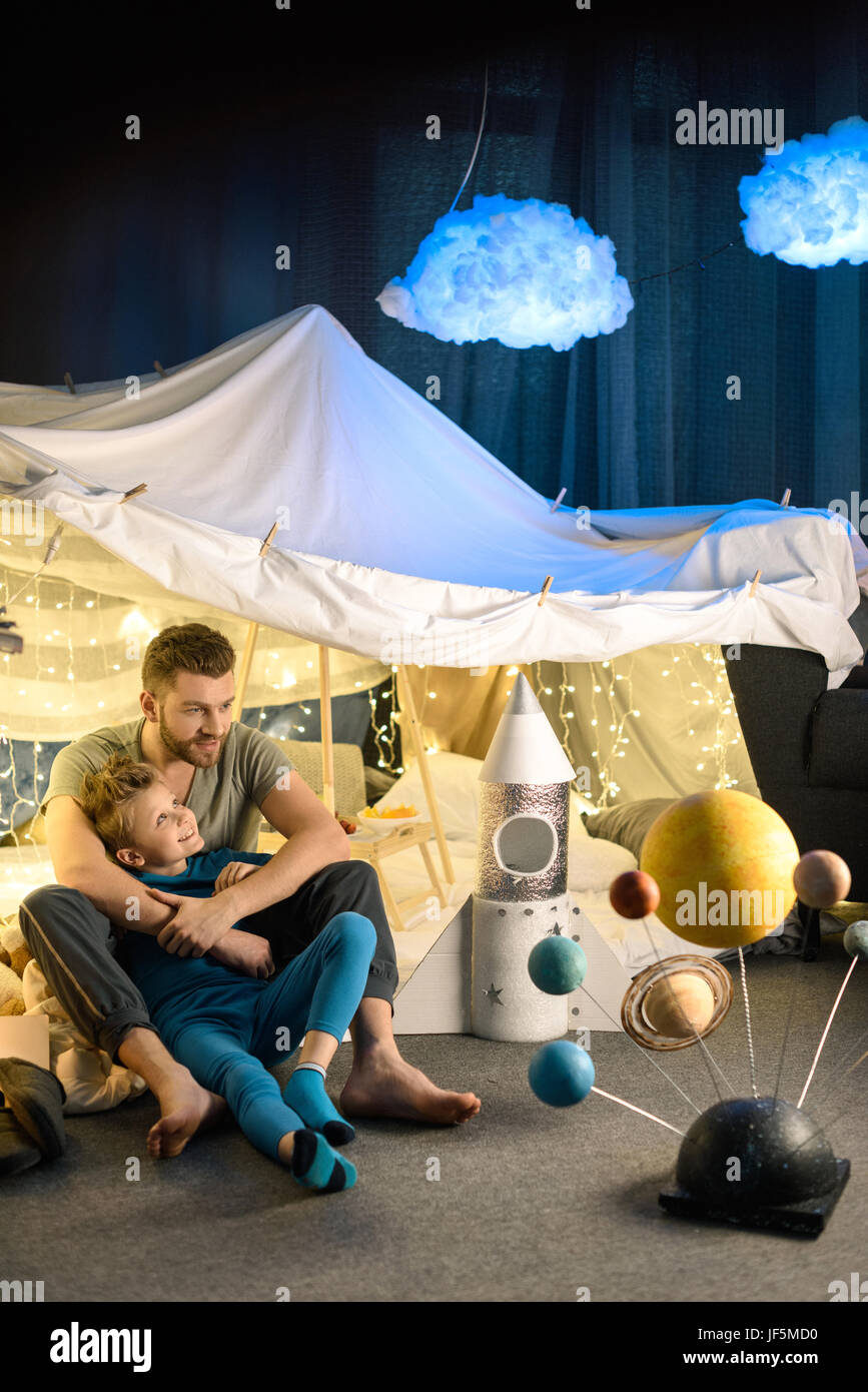 father and son sitting together in blanket fort with toy rocket and solar system model Stock Photo