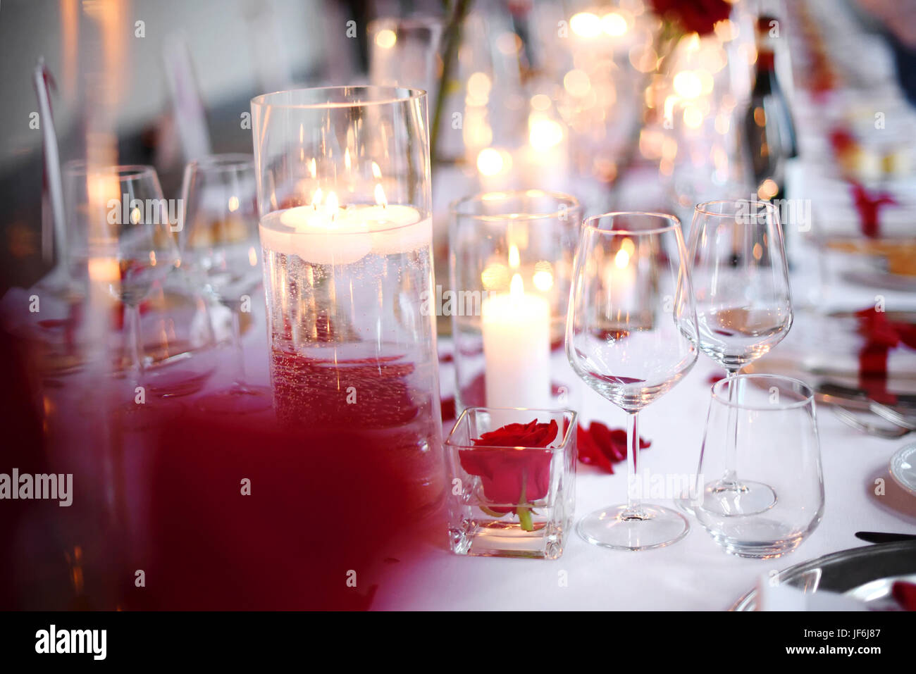 Romantic candlelit dinner table setting with elegant glassware and red flowers over a white tablecloth in a close up view Stock Photo