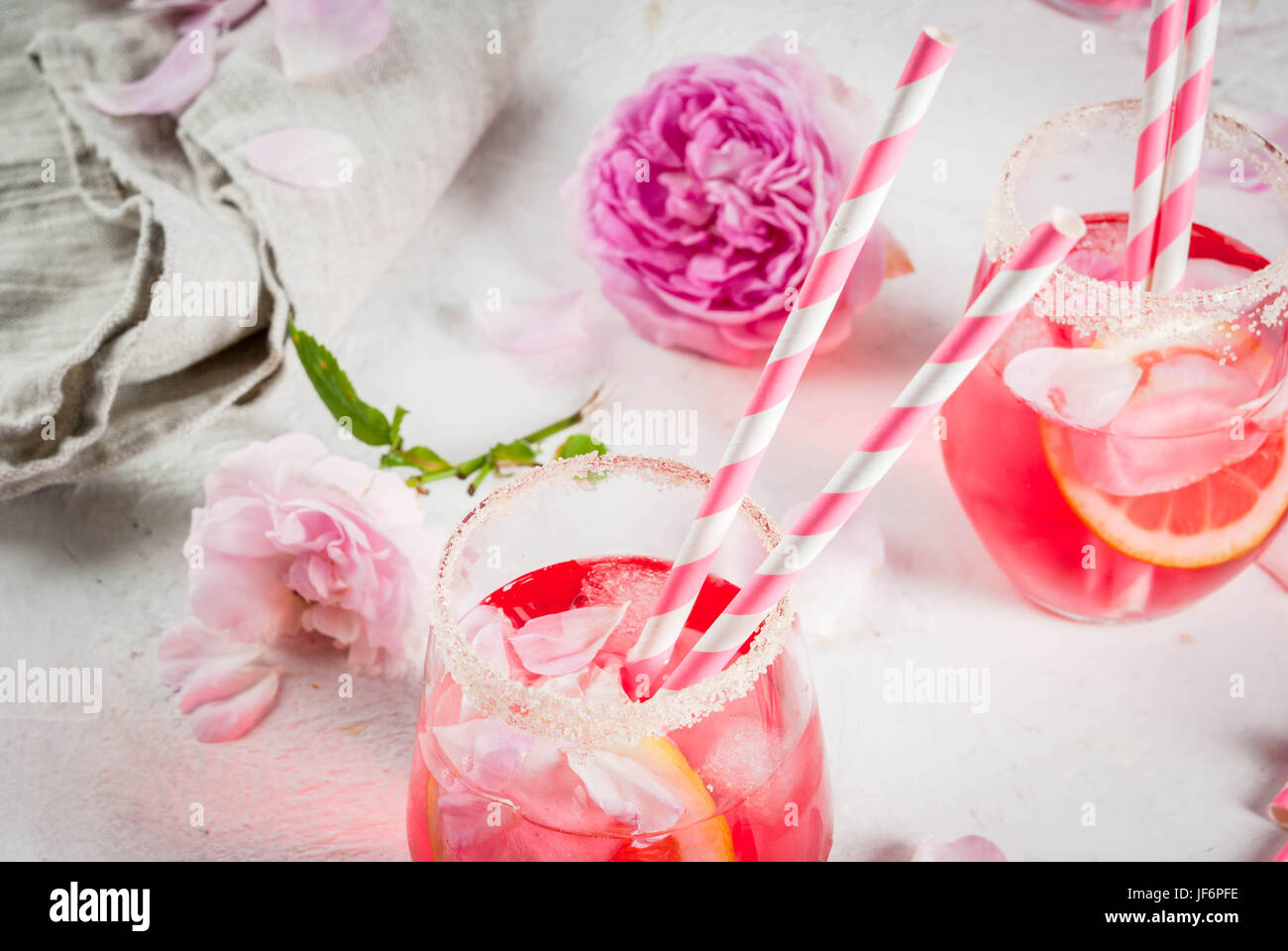 Summer refreshment drinks. Light pink rose cocktail, with rose wine, tea rose petals, lemon. On a white stone concrete table. With striped pink tubule Stock Photo