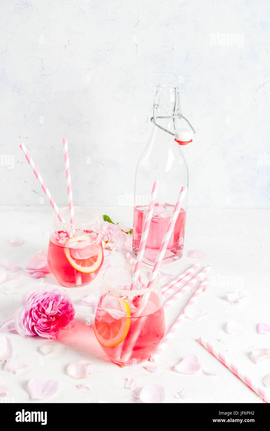 Summer refreshment drinks. Light pink rose cocktail, with rose wine, tea rose petals, lemon. On a white stone concrete table. With striped pink tubule Stock Photo