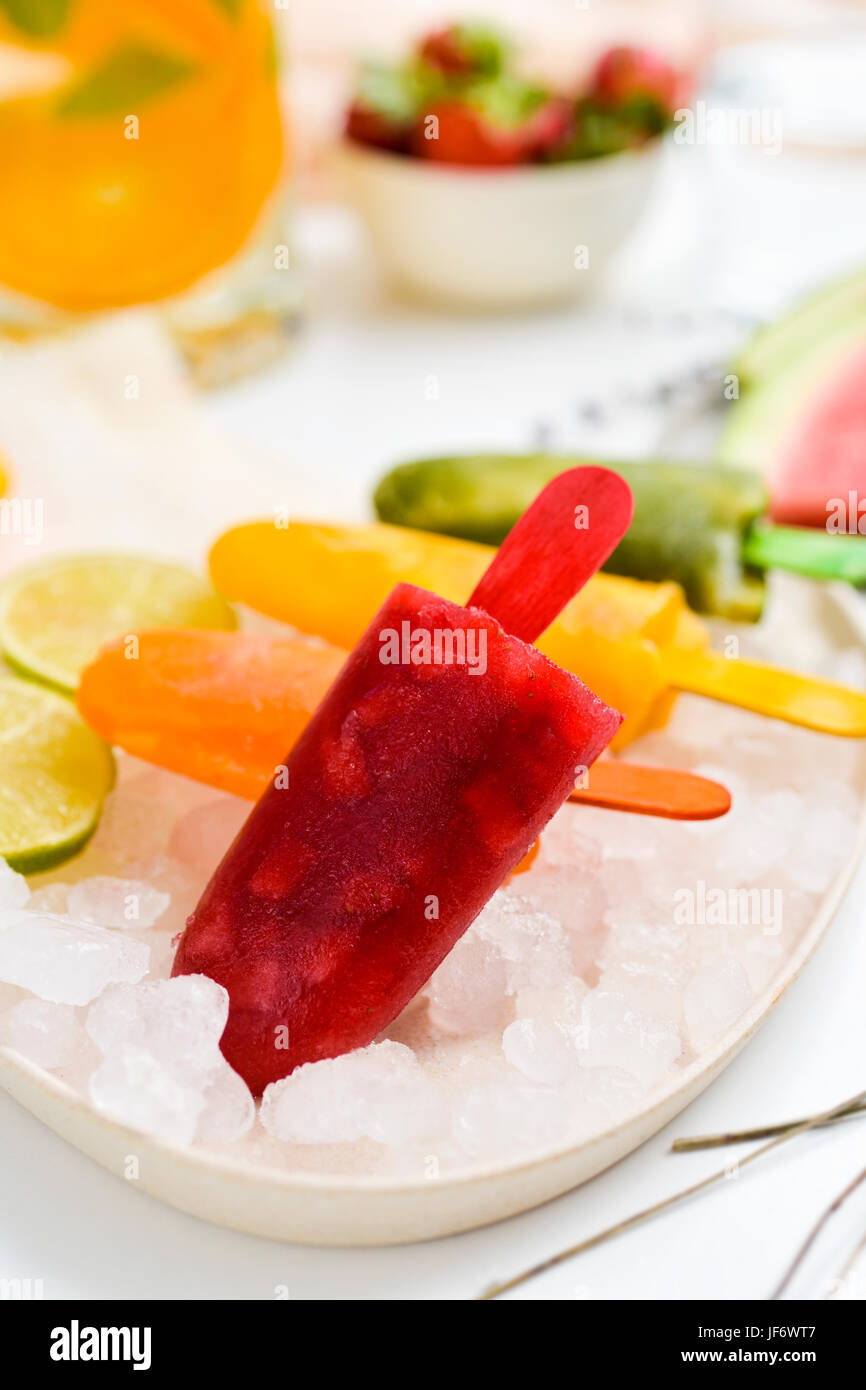 some different homemade natural ice pops made with natural fruit juices and pieces of fruit in a plate with ice, placed on a table Stock Photo