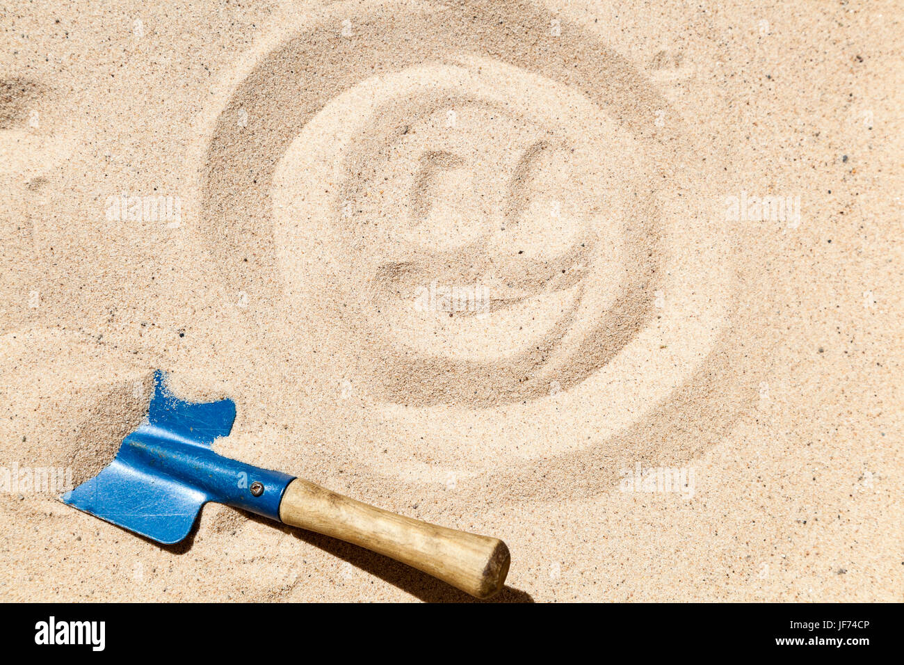 Smiley face drawn on sand and a small blue spade Stock Photo