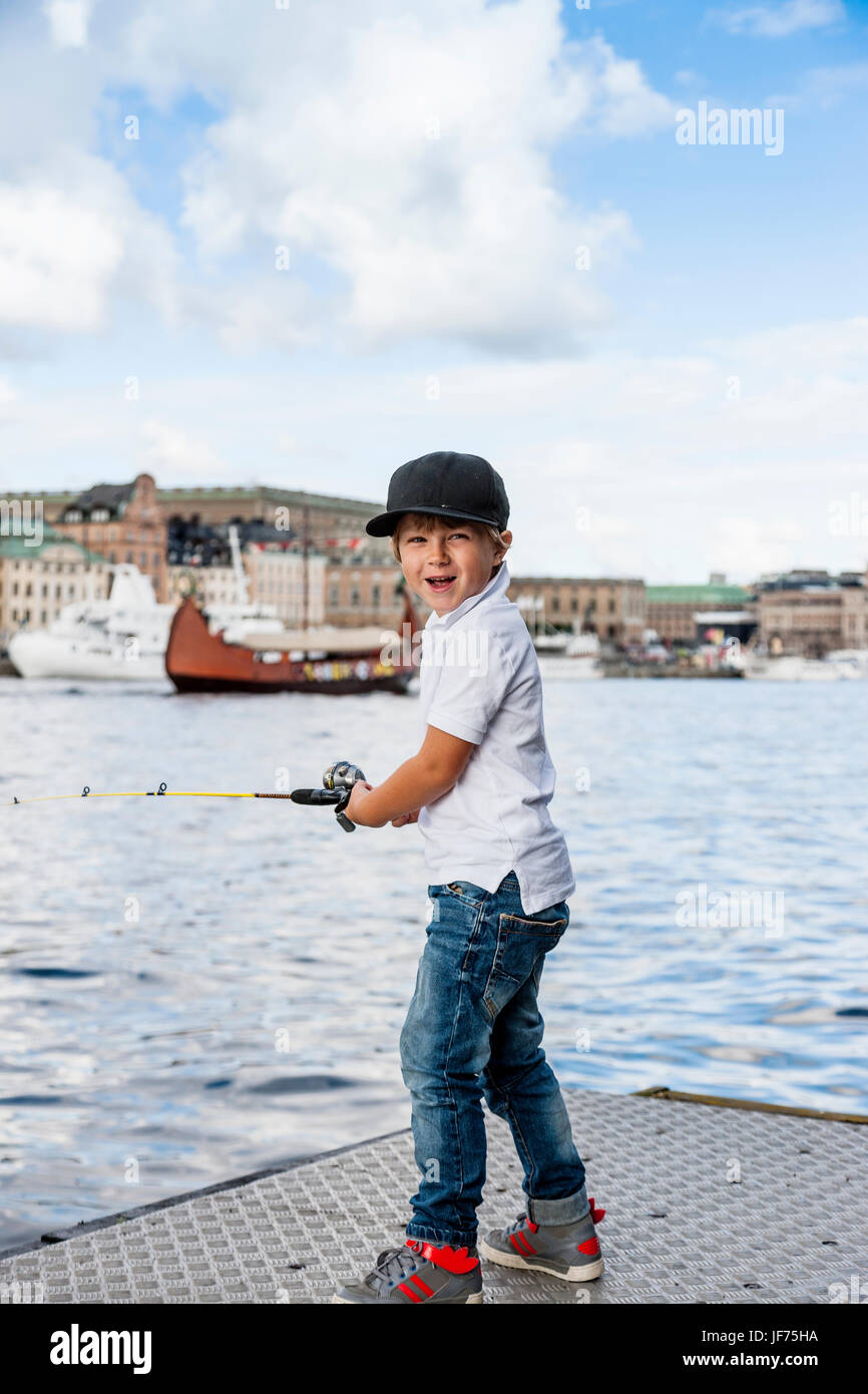 Portrait of boy fishing in river, old town in background Stock Photo