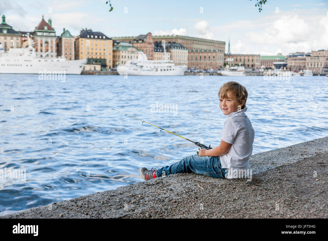 Portrait of boy fishing in river, old town in background Stock Photo