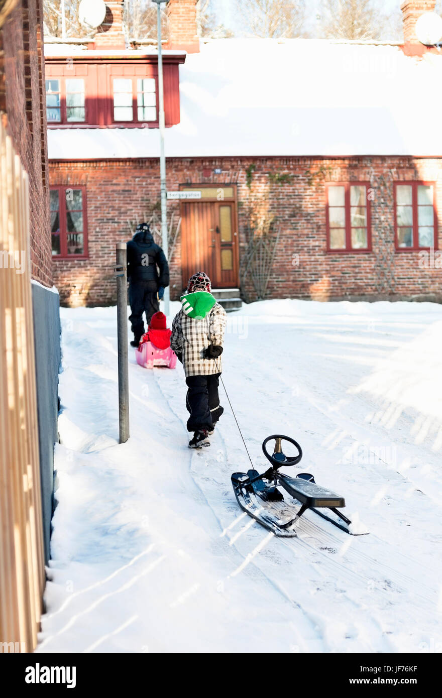 Rear view of woman with children walking and pulling sleigh Stock Photo ...