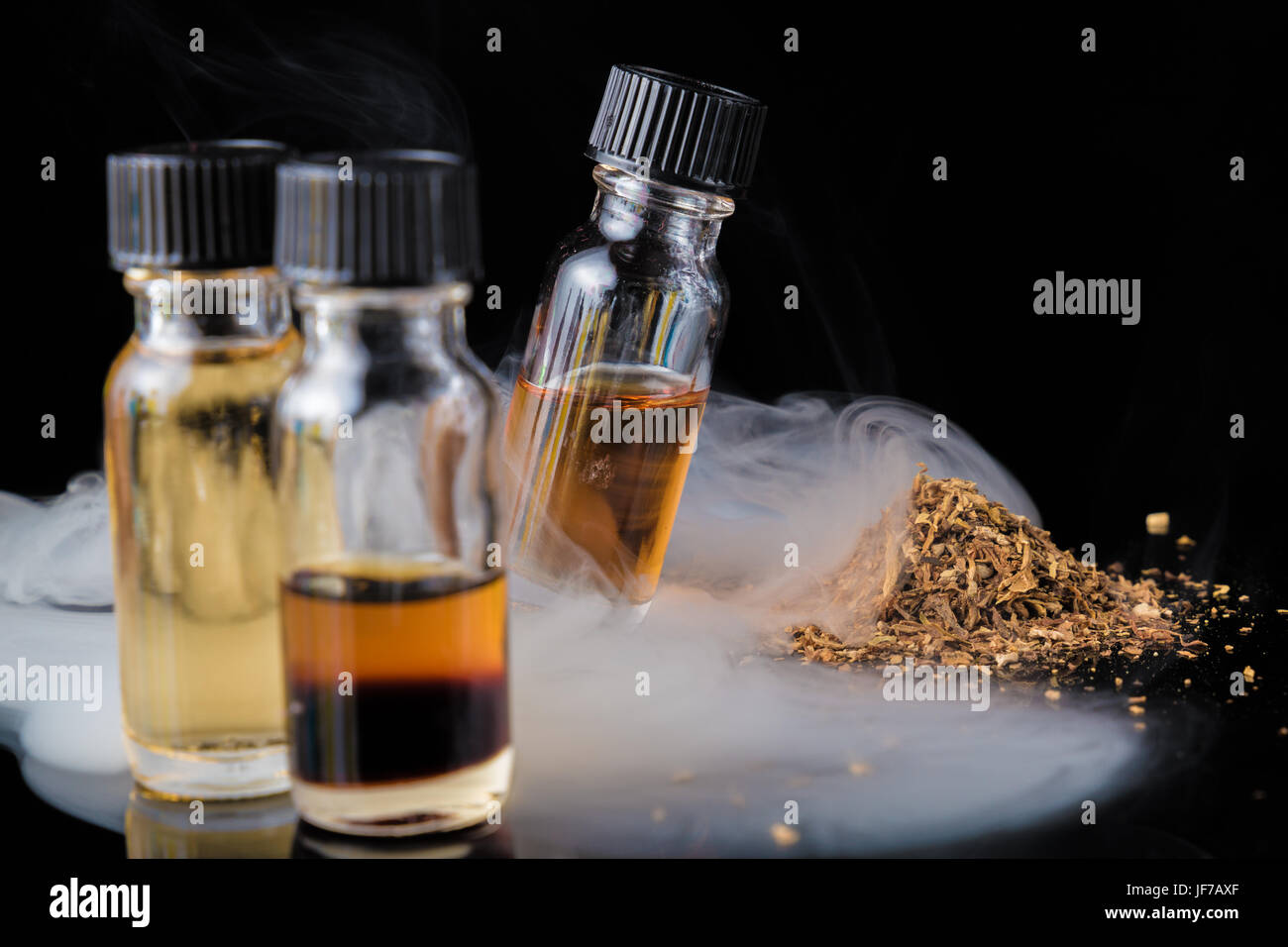 E-liquid bottles next to grinded tobacco leaves and smoke cloud Stock Photo