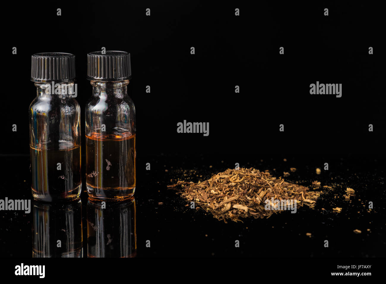 E-liquids next to pile of grinded tobacco leaves Stock Photo