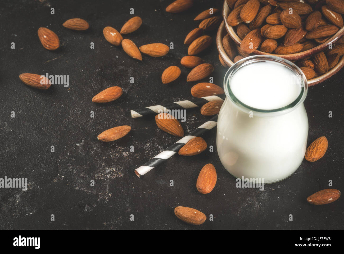 Vegetable sources of protein. Vegan healthy food. A small bottle of almond milk, portion. Against the backdrop of nuts, almonds, on a black concrete t Stock Photo