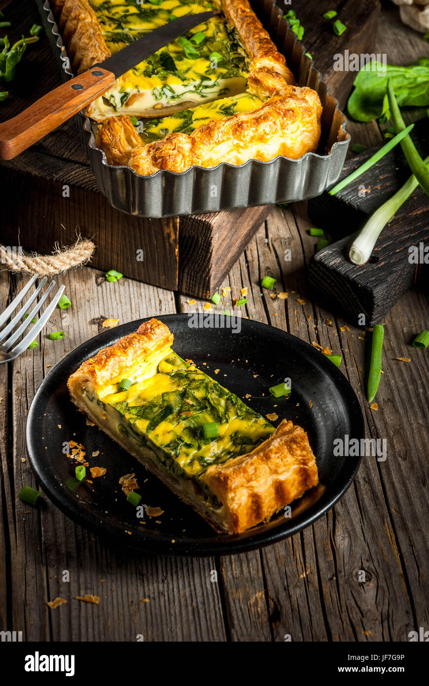 French home cooking. Casserole. Pie. quiche lorraine from puff pastry, with young green onions and spinach. On old wooden rustic table. Cut. In form f Stock Photo