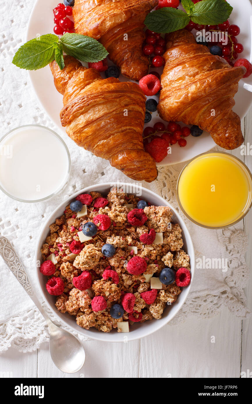 Healthy breakfast: granola with berries and croissants, milk and orange juice close-up on the table. vertical view from above Stock Photo