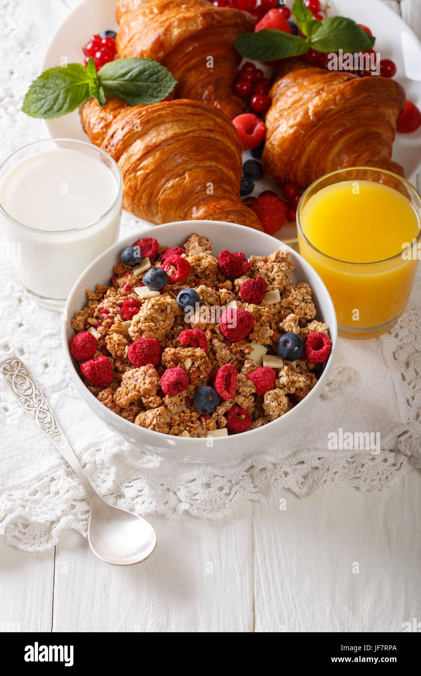 Healthy food: multigrain granola, croissants, fresh berries, milk and orange juice close-up on the table. vertical Stock Photo