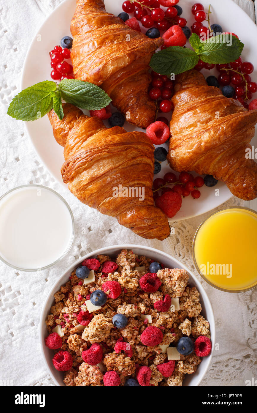 Healthy food: granola, croissants, fresh berries, milk and orange juice close-up on the table. Vertical view from above Stock Photo