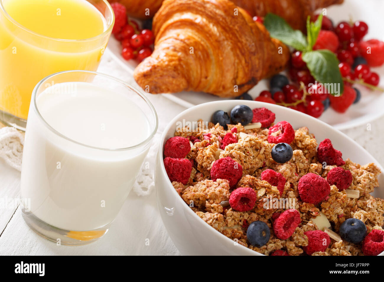 Baked granola with berries, as well as croissants, milk and juice close-up on the table. horizontal Stock Photo