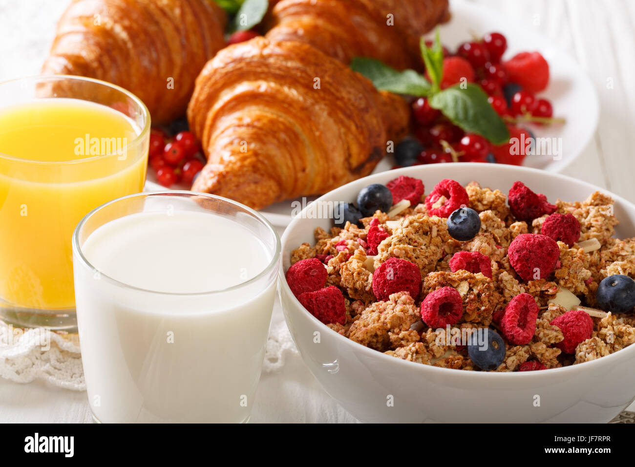 Delicious breakfast of granola with berries, as well as croissants, milk and orange juice close-up on the table. horizontal Stock Photo