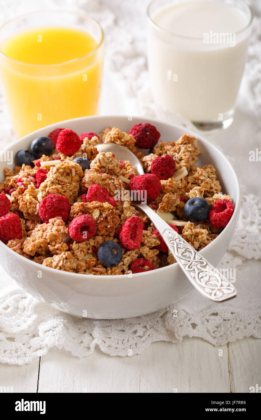 Baked granola with dried raspberries and blueberries, milk and juice close-up on a table. vertical Stock Photo