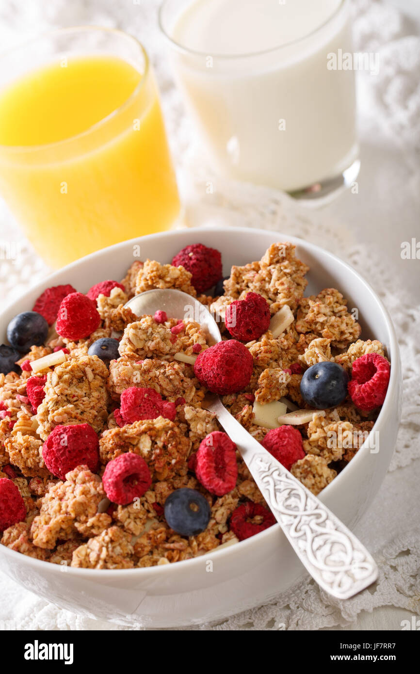 Multigrain granola with dried raspberries, nuts and blueberries, milk and juice close-up on the table. vertical Stock Photo