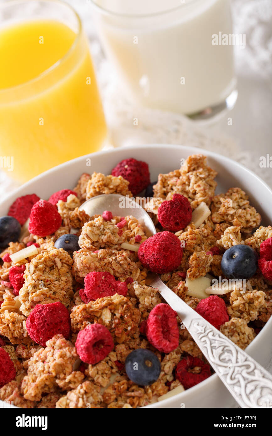 Delicious breakfast of granola with dried raspberries, nuts and blueberries, milk and juice macro on the table. vertical Stock Photo