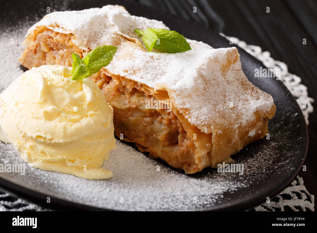 Apple strudel sprinkled with powdered sugar with ice cream and mint closeup on a plate. horizontal Stock Photo