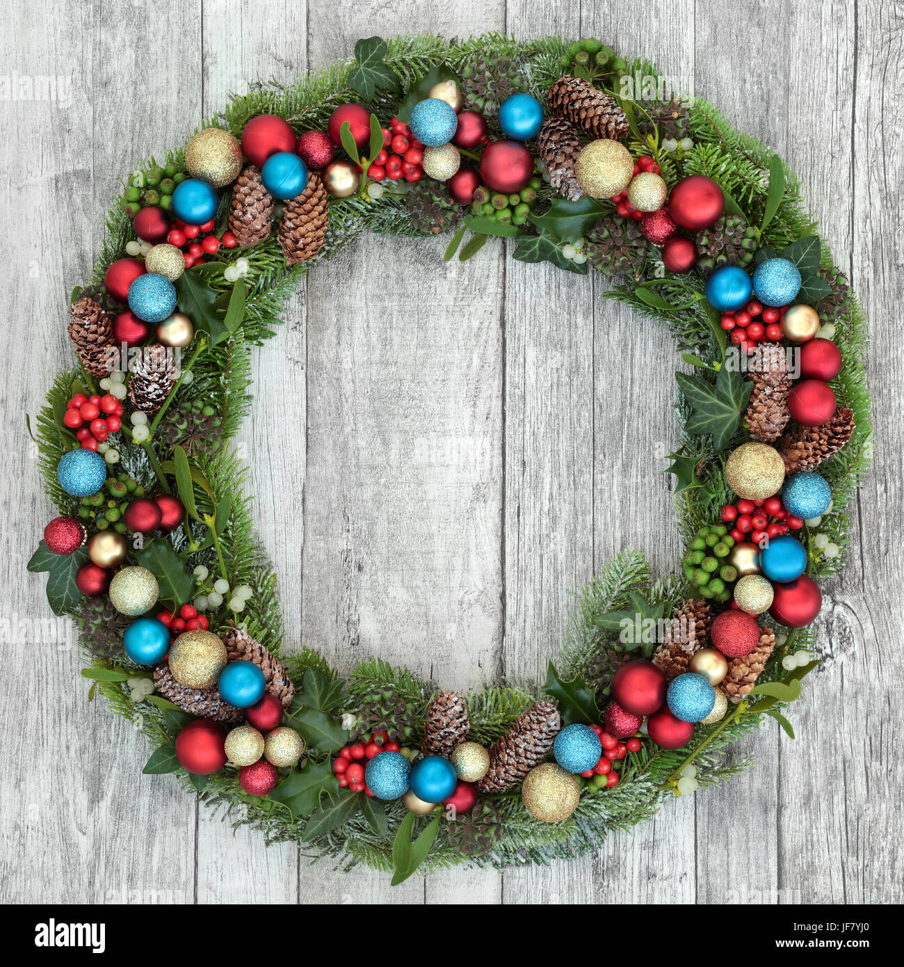 Christmas wreath decoration with red, gold and blue baubles, holly, mistletoe, fir, blue spruce, ivy and pine cones on distressed white wood backgroun Stock Photo